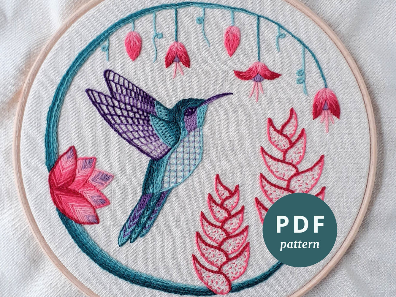 Crewelwork embroidery of a green and purple hummingbird surrounded by pink flowers.
