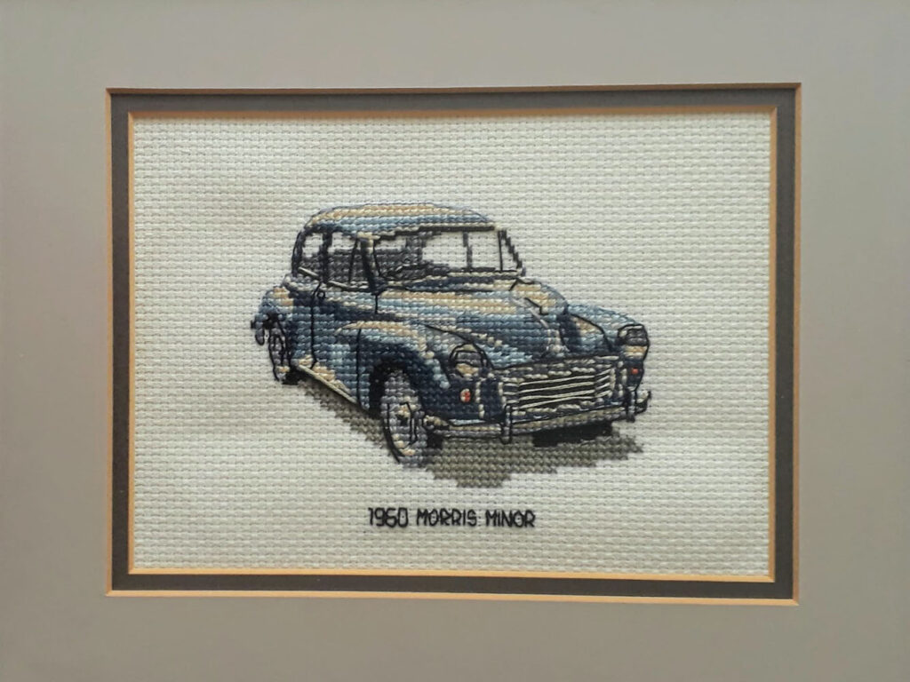 Cross stitch of a blue Morris Minor in a light grey mount.