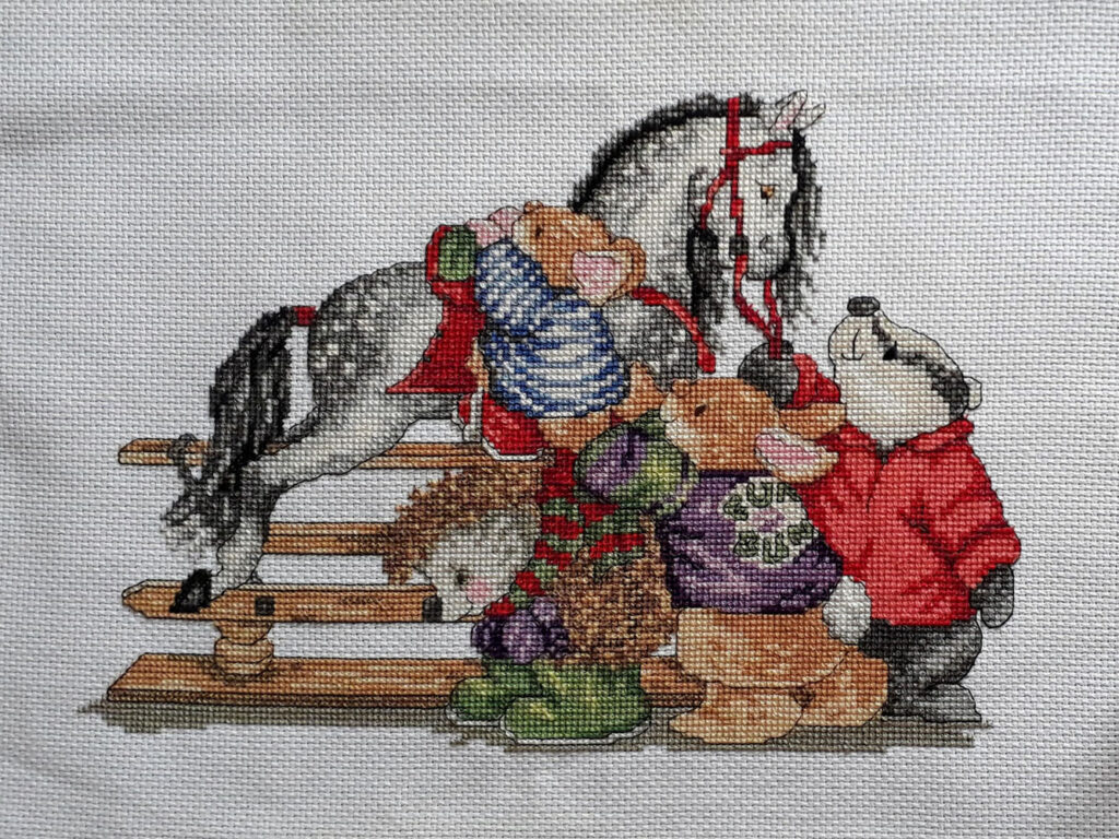 Cross stitch picture of a badger, hedgehog and couple of bunnies with a rocking horse.