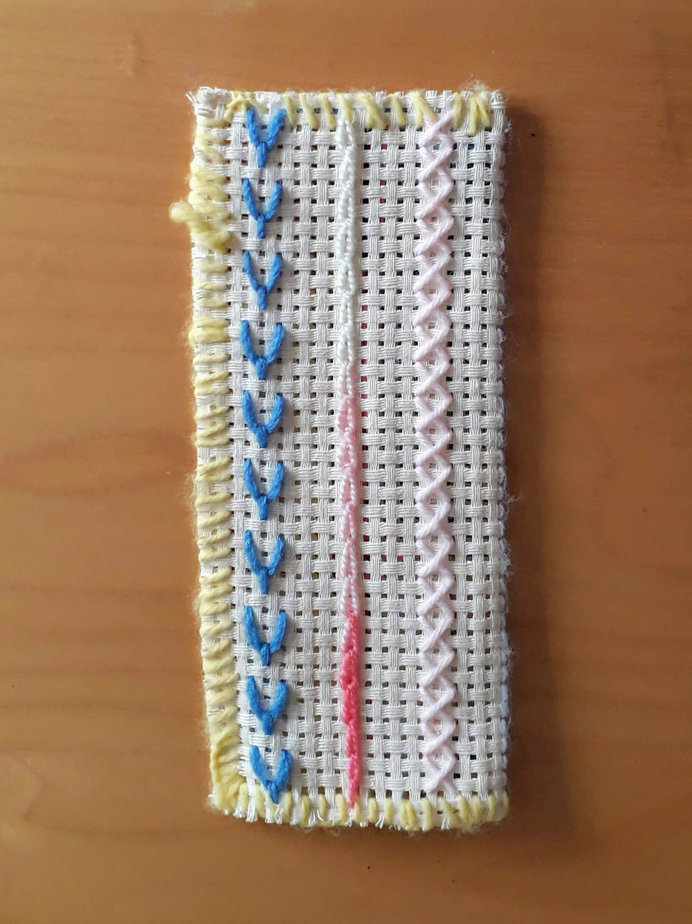 A comb holder with stitch samples in blue, pink and yellow thread.