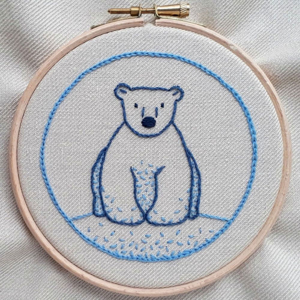 Embroidery of a cute polar bear sitting face on, stitched in shades of blue crewel wool.
