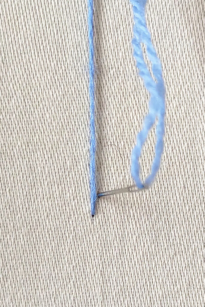 Thread lying vertically on fabric, with the needle going down to the right of the thread.