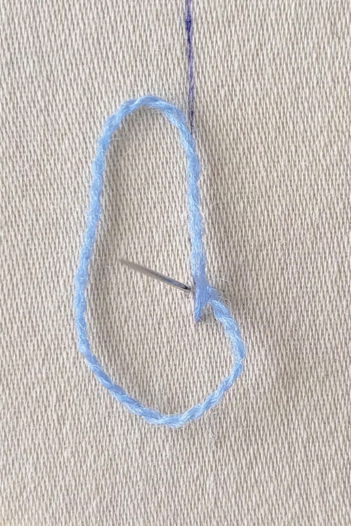 Needle coming up inside a loop of thread.