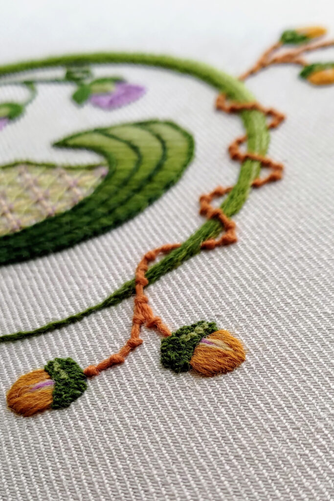 Brown crewel embroidery vine in coral stitch wrapping around a green stem.