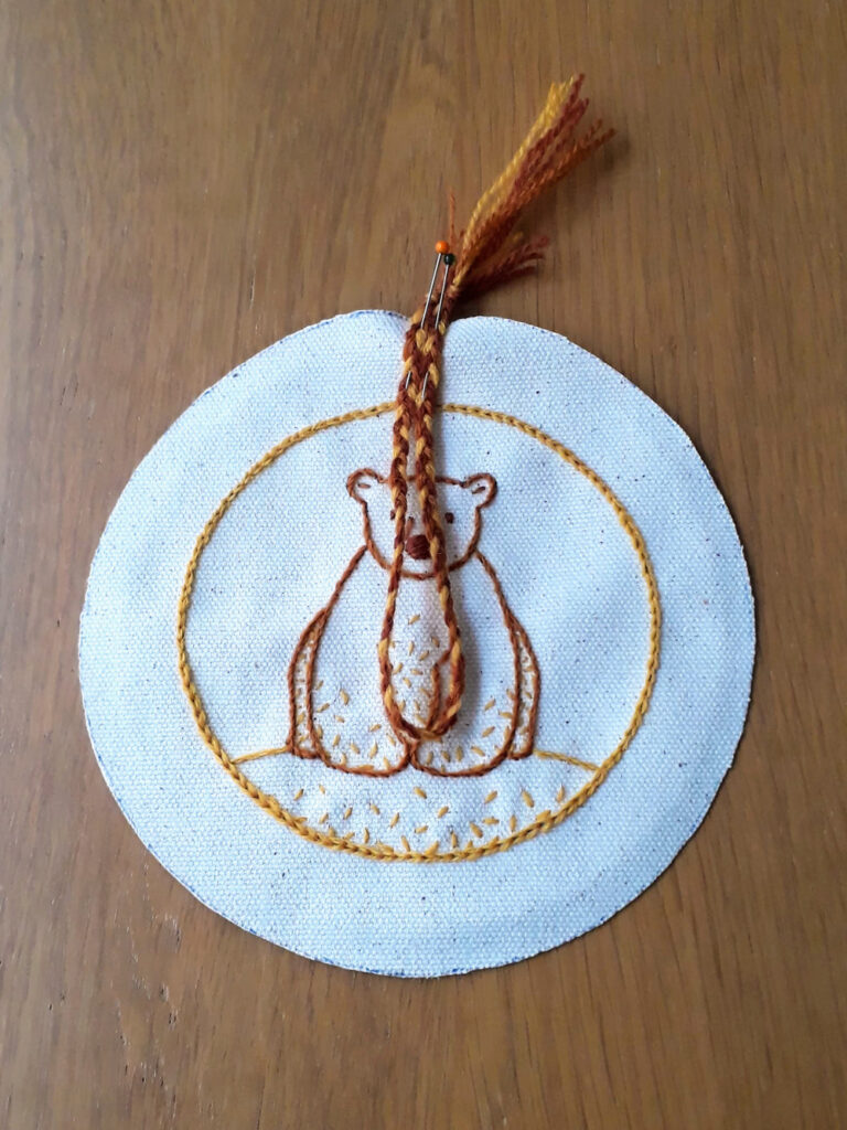 A folded thread braid pinned to the top of an embroidered circle of fabric.