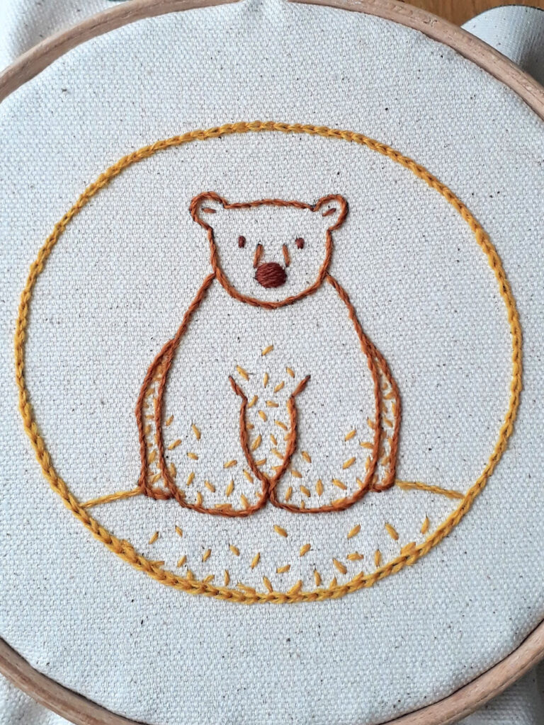 Crewel embroidery of a cute bear stitched with yellow and brown crewel wools.