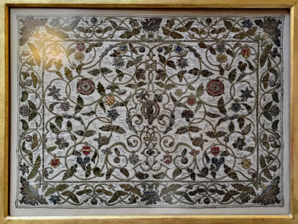 A framed embroidery densely stitched with scrolling vines and flora and fauna. The embroidery is worked in a combination of goldwork and crewelwork.