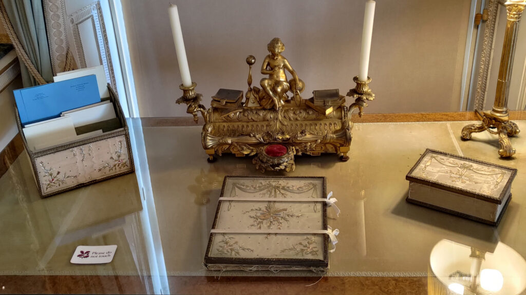 Photo of the top of a desk upon which is a set of embroidered stationary items along with an ornate candle holder.
