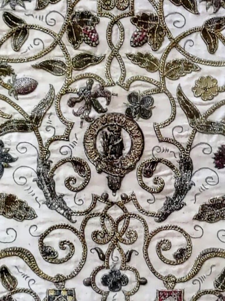 Close up of goldwork and crewelwork embroidery of flora and fauna motifs surrounding a central motif that could be the bear and staff of Warwickshire.