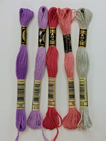 Stranded cotton skeins lined up next to each other. A couple of purples, a couple of coral pinks and a light green/grey.