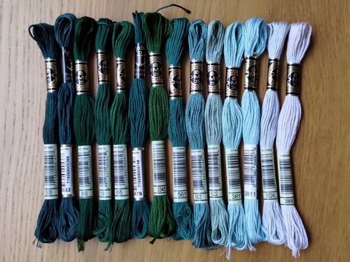 A selection of stranded cotton skeins lined up next to each other by tone in shades from dark to very pale green.