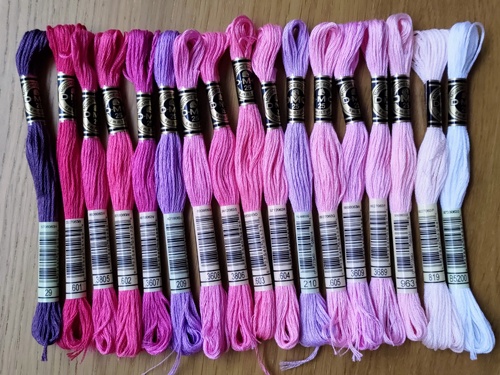 A selection of stranded cotton skeins lined up next to each other by tone in shades of purples and pinks.