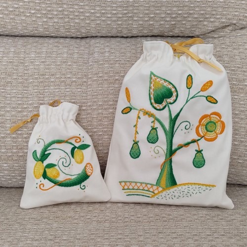Photo of one large and one small embroidered gift bags. The embroidery on the small bag is of lemons within a circular stem. On the larger bag the embroidery features pears on a tree of life design.