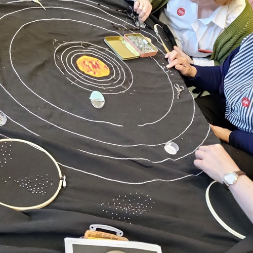 A group of people working on the solar system quilt together.