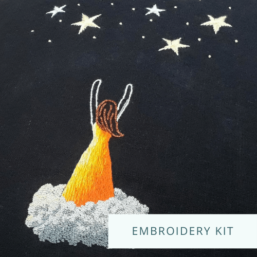 Embroidery of a woman in an orange dress standing on a cloud reaching up towards stars. Text overlay says "Embroidery kit".