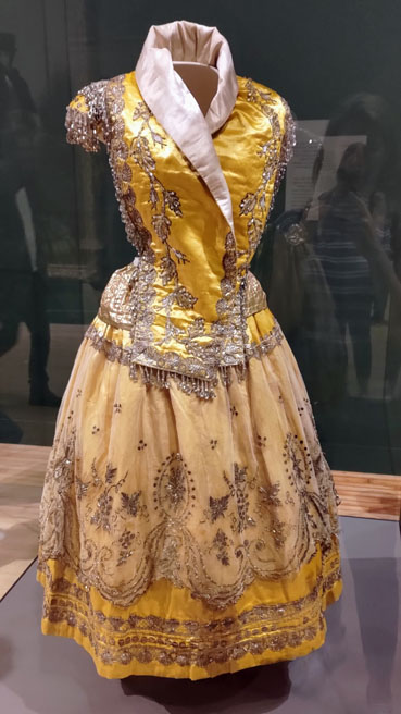 Sleeveless dress with high white collar, with lots of embroidered detail.