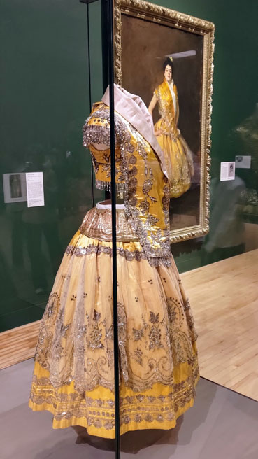 Gold embroidered bolero and skirt in the foreground. Portrait with the outfit being worn in the background.