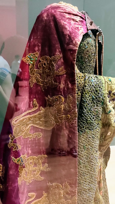 Side view of the Lady Macbeth outfit showing the red cape with gold lions embroidery.