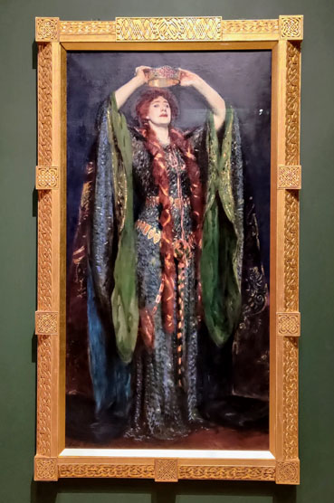 Painting of a white woman with long red hair wearing a dramatic blue and green dress while holding a crown above her head.