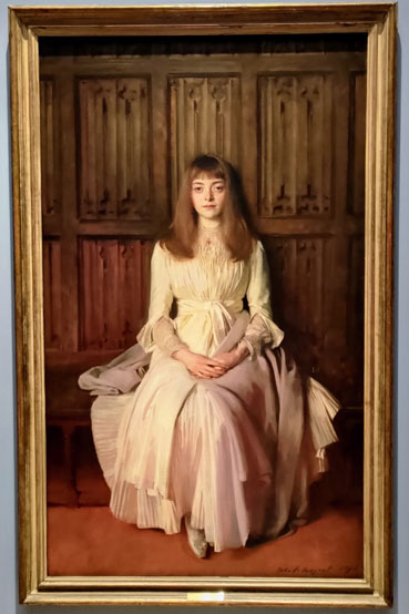 Painting of a seated woman surrounded by wooden panels, wearing a white dress with a pale lavender shawl draped across her lap.