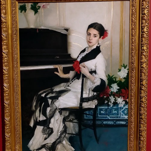 Painting of a white woman sat at a piano wearing a white and black outfit with a red flower in her hair and one at the front of her jacket.
