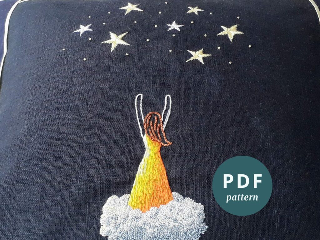 A completed embroidery of a woman standing on a cloud reaching up towards stars. In the lower right of the image is a sticker with the text 'PDF pattern'.
