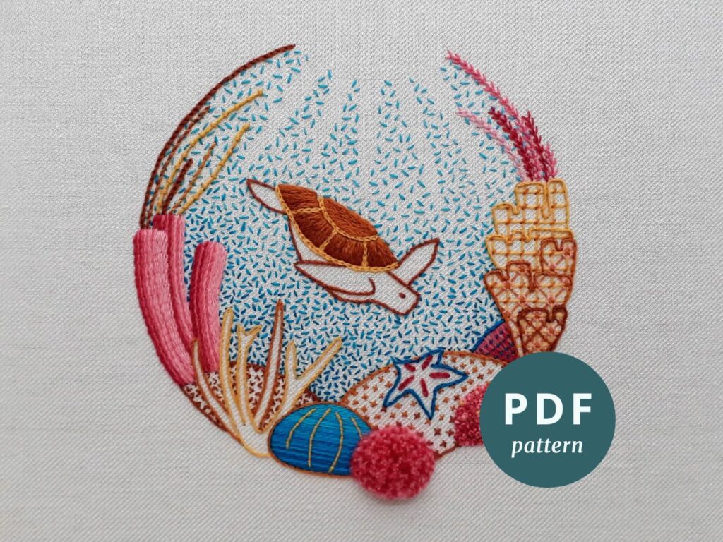 A completed crewelwork embroidery of turtle swimming amongst coral. A sticker in the lower right says 'PDF pattern'