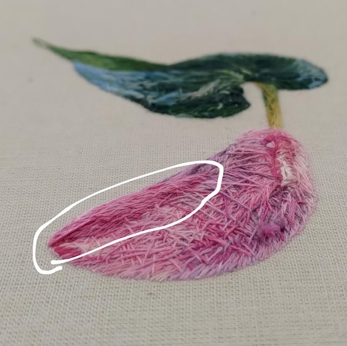 The back of a finished silk shading embroidery of a pink peace lily. The photo is angled to show the area where padding was created out of threads.