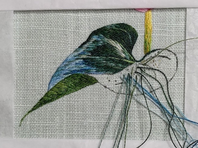 A leaf that's half filled in with silk shading embroidery using various shades of green, blue and grey threads.