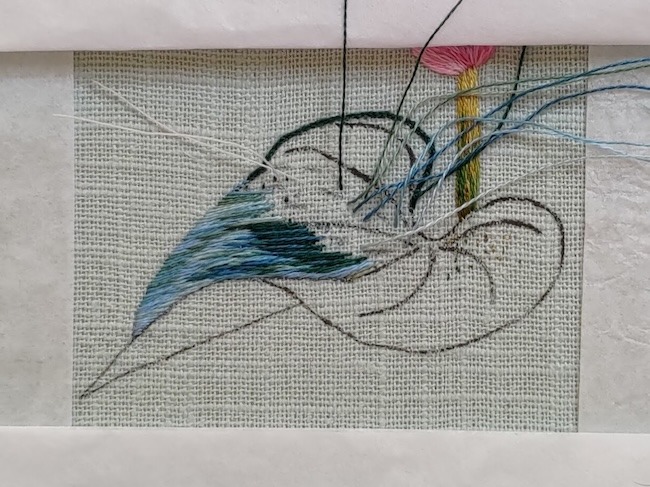 Photo of leaf being stitched with silk shading embroidery. To the left, the stitches are blue-greens and darker greens are being added to the right.