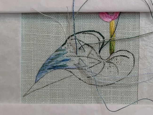 Photo of a little bit of silk shading embroidery on part of a leaf, the colours look mainly shades of light blue-green.