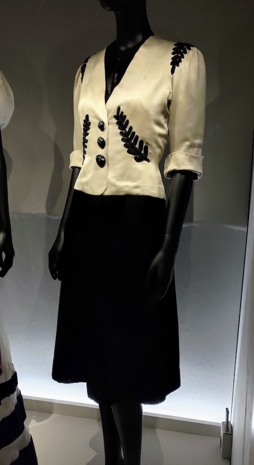 Photo of a skirt suit with black skirt and white jacket with black buttons and fern like embellishments.