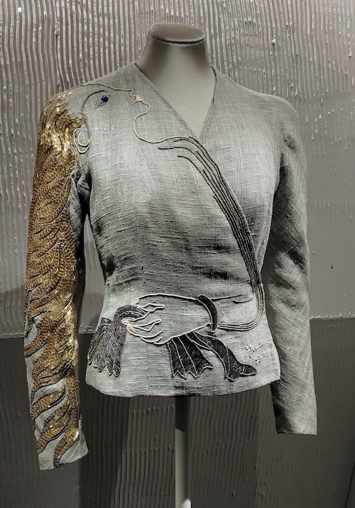 A grey wrap over jacket with lots of gold on one sleeve and embroidery on the front to make this look like the flowing hair of a woman.