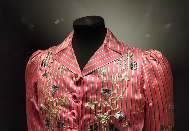 Photo of the top part of a pink striped jacket. The collar uses pleats to create the look of a classically tailored collar.