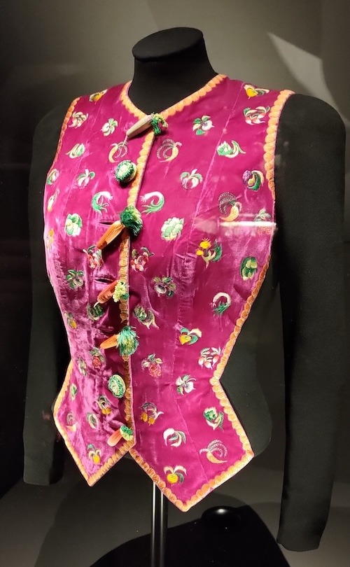 Photo of jacket with a bright pink front covered in embroidered vegetable motifs and with buttons shaped like different vegetables.